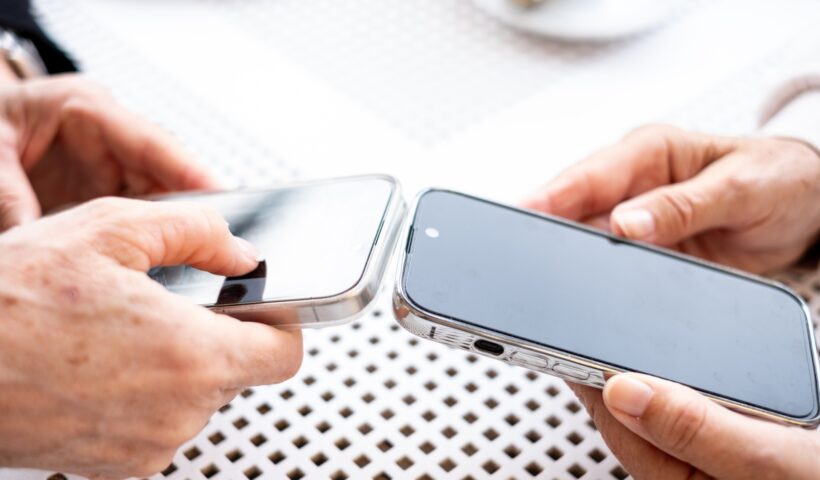 Close up view of two modern women's hands using apps and wireless technology to share files