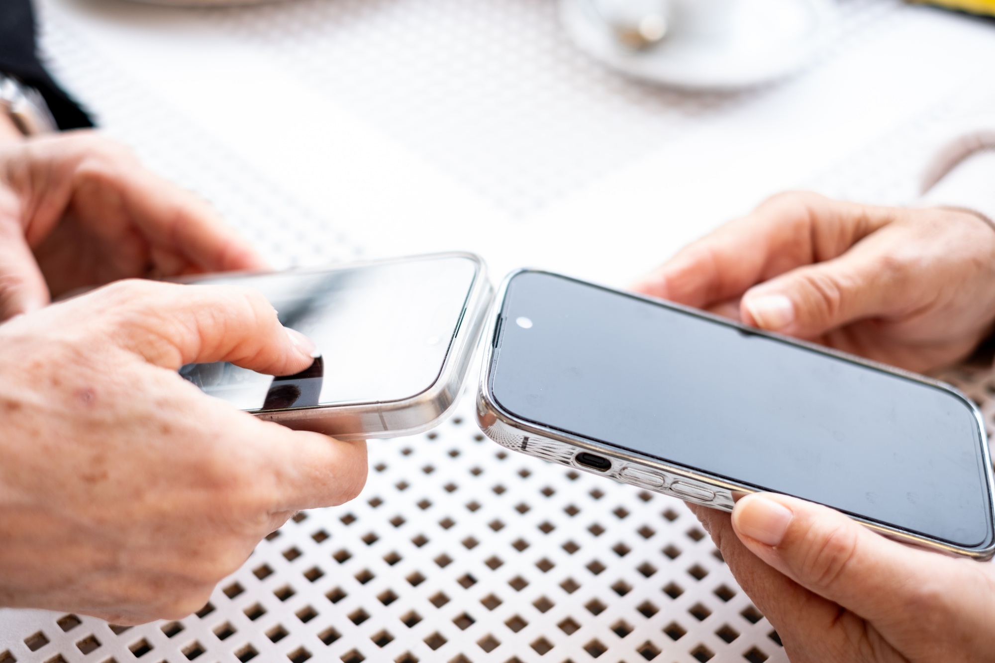 Close up view of two modern women's hands using apps and wireless technology to share files